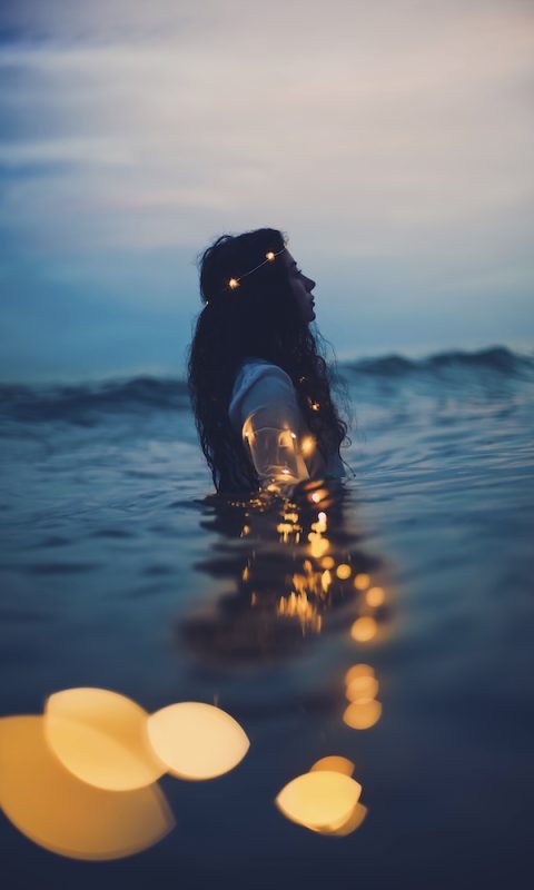 Girl in the sea in the dusk time with lights around